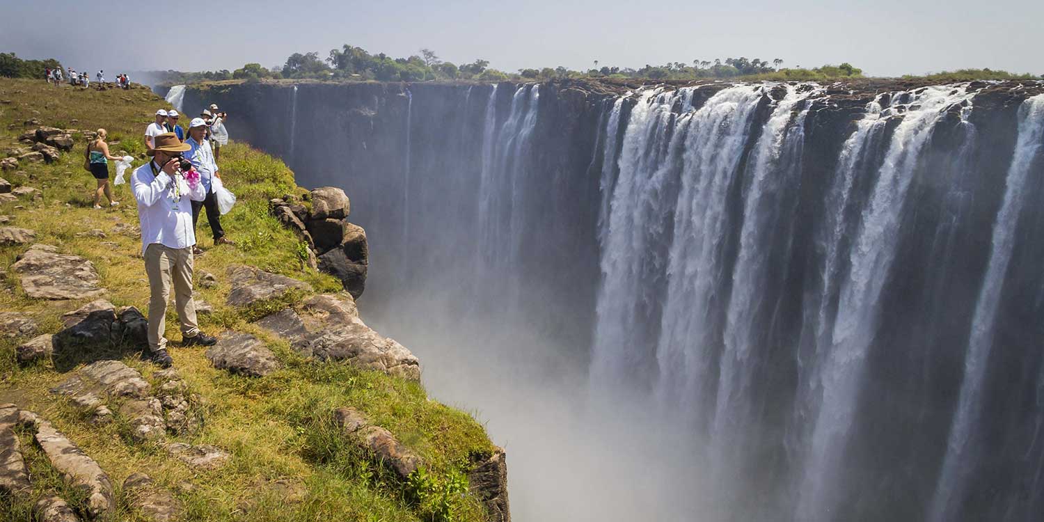 tourists take photos next to Victoria Falls