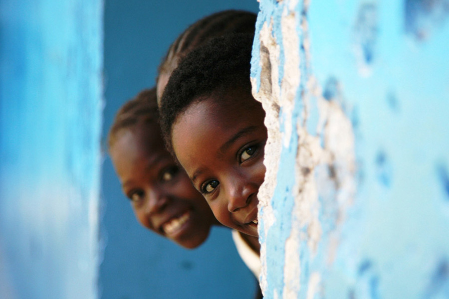 three young children peek head out of wall for photo