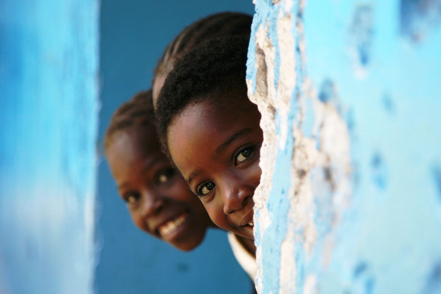 three young children peek head out of wall for photo