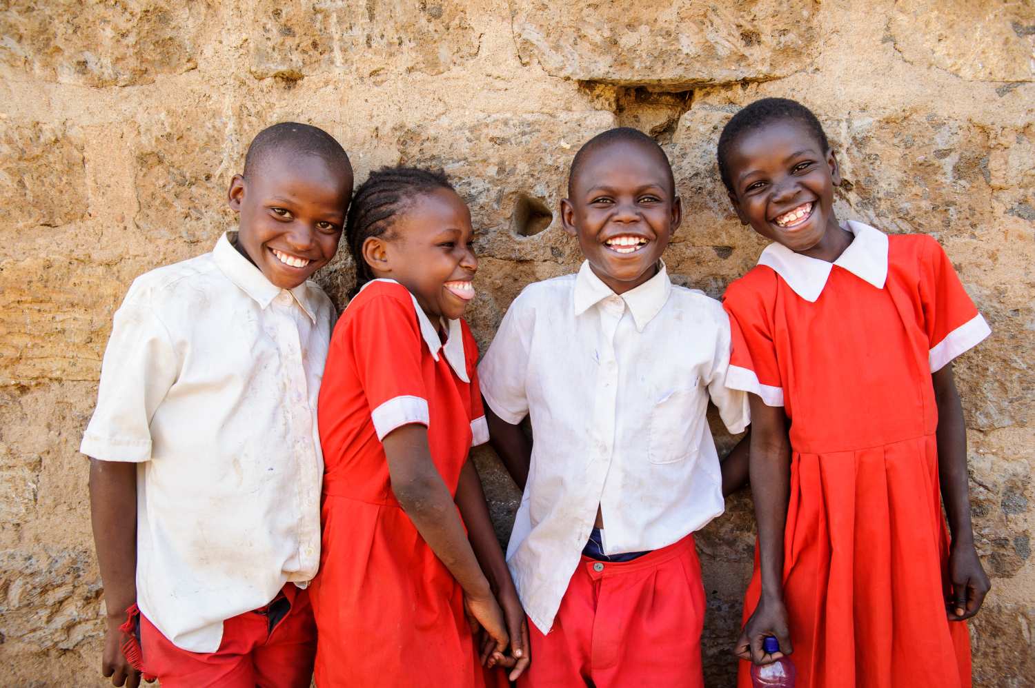 four smiling children in red and white school uniform